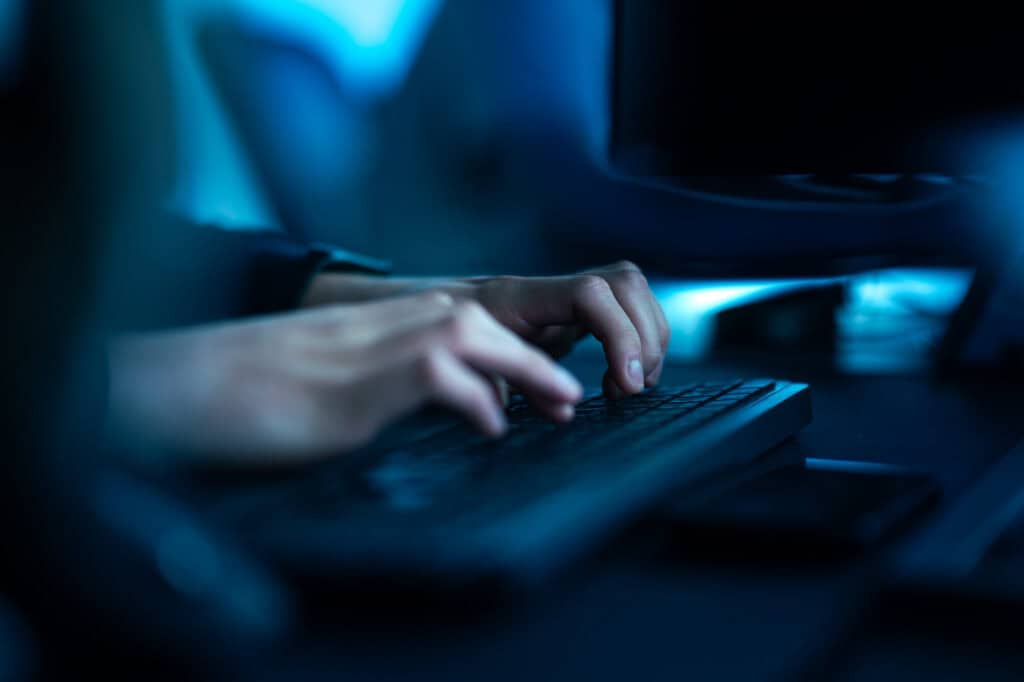 Hender som arbeider ved et tastatur i et blåbelyst IT-miljø.